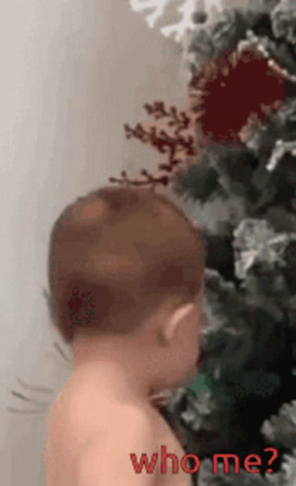 a baby standing in front of a christmas tree with the words who me written on it