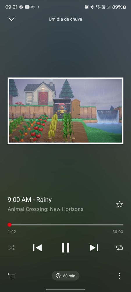 Captura de tela do aplicativo Nintendo Music tocando a música "9:00 AM - Rainy" de Animal Crossing: New Horizons da playlist "Um dia de chuva". A música possui 60 minutos de duração e está no comecinho. A imagem de capa da música mostra uma ilha de Animal Crossing em um dia chuvoso, com uma horta farta à frente, um rio com uma pequena queda d'água à direita, um personagem humano vestindo uma capa de chuva amarela com chapéu cor-de-rosa, sentado em um banco de madeira sob um pequeno telhado, e ao fundo uma pequena casa na colina com dois pinheiros.