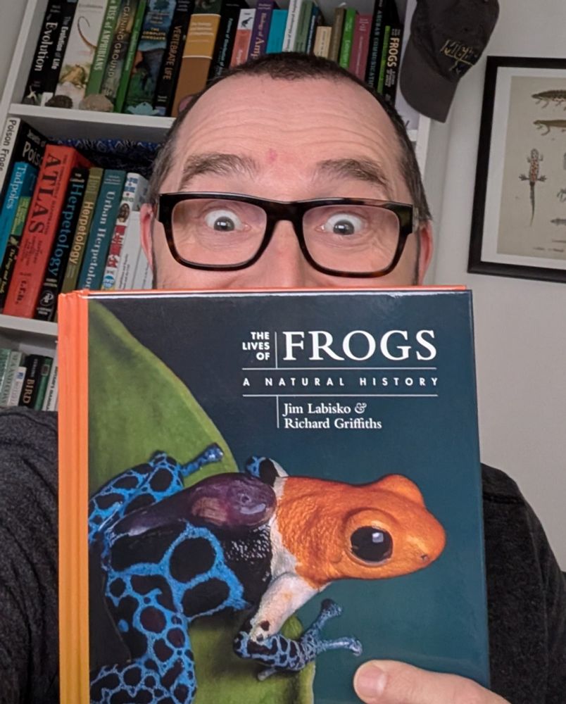 The author of a new book on frogs holding a copy, showing the cover which depicts a fantastic poison frog (Ranitomeya fantastica) carrying a tadpole on its back.