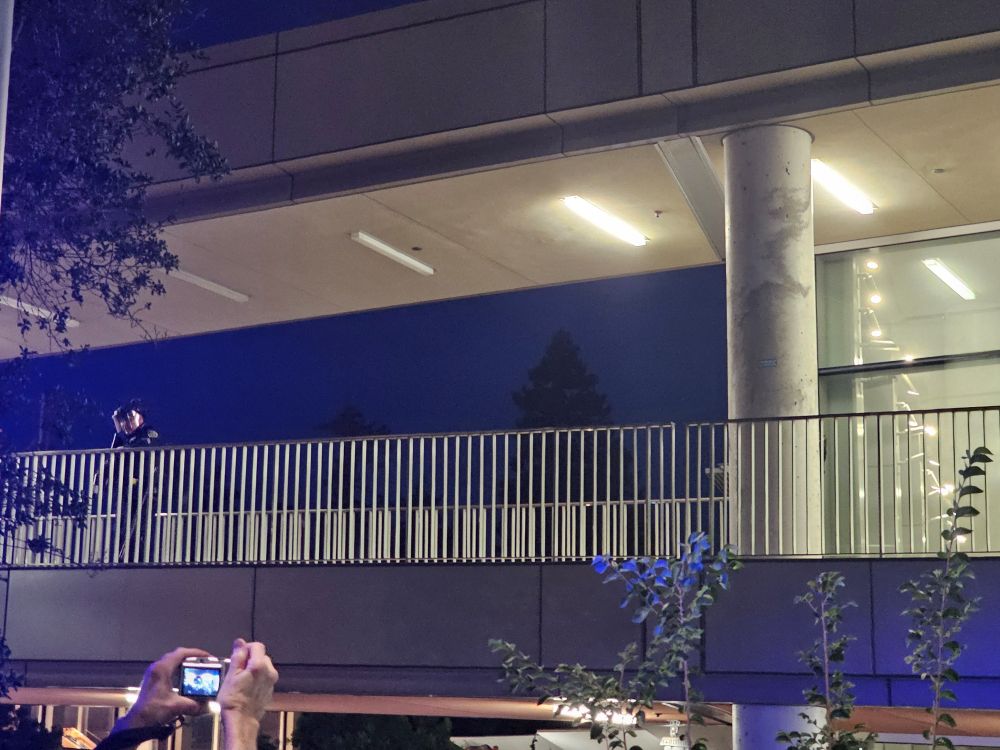 An officer stands on the left side of the overhead walkway. He is wearing a helmet and has a lethal lethal launcher for PepperBalls