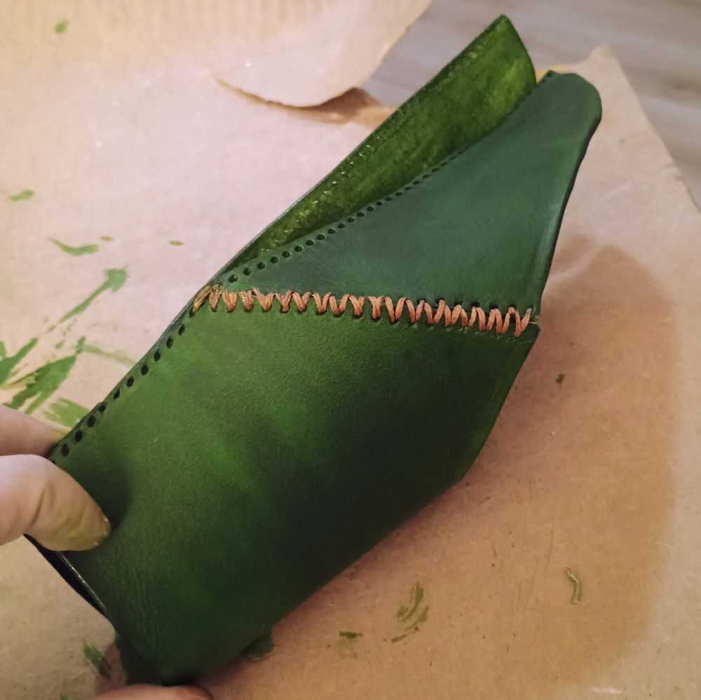 Side view of a green leather forearm guard. Two pieces are stitched together but the main length remains unstitched.