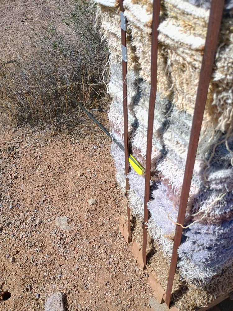 An arrow is stuck between the straps and the side of the archery target 