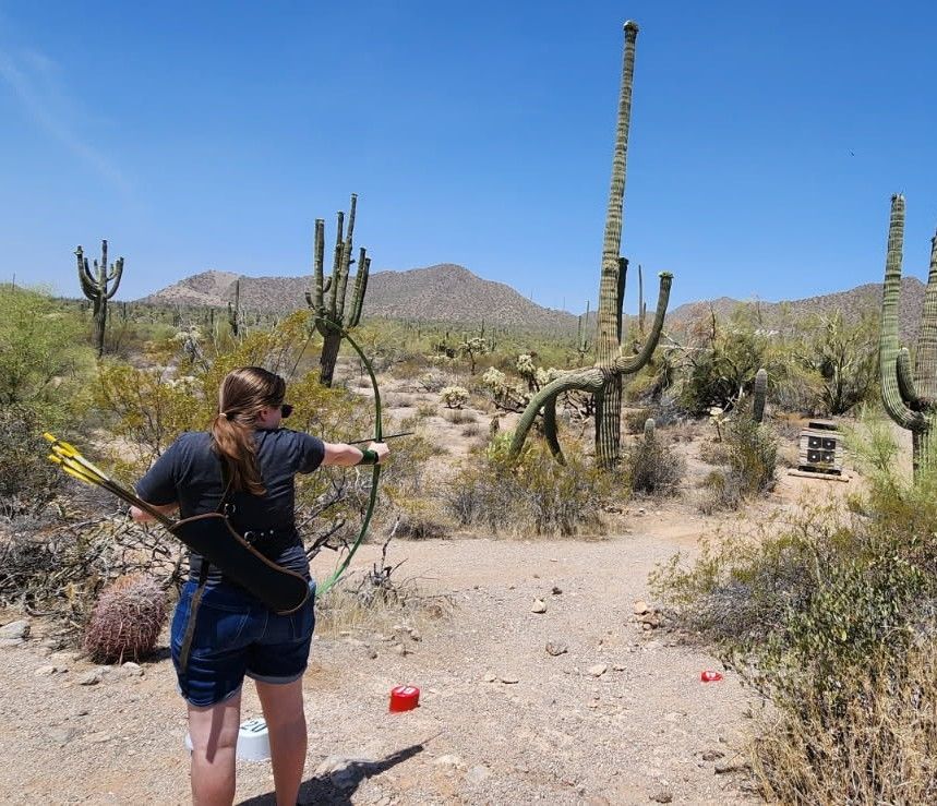 Photo of a woman with her back to the camera, drawing an arrow on a recurve bow. 