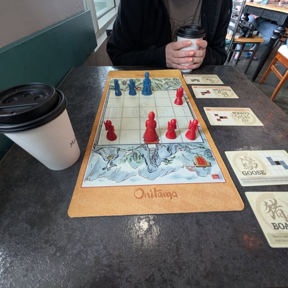 A game of Onitama with coffee next to it.