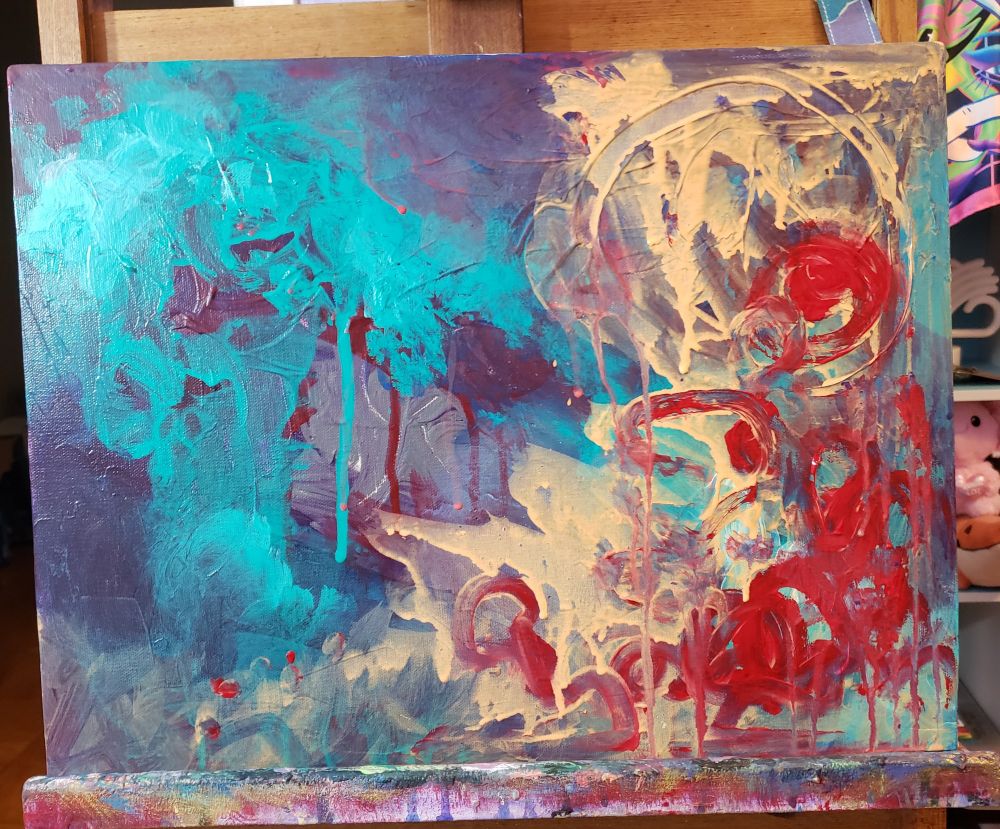 A painting sits horizontally on an easel. It has swirls of turquoise, tan, and red acrylic paint. Some of the paint is mixed together with a brush and some is dripping. 