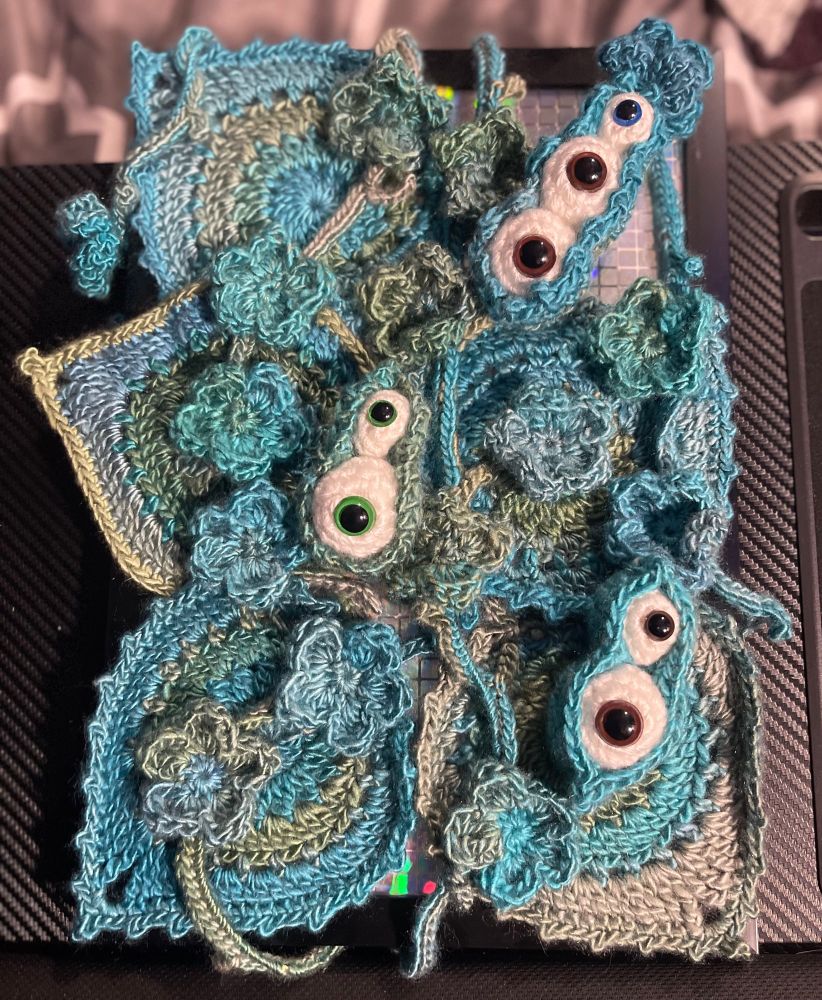 Crochet collage of leaves, vines, flowers, and pea pods full of eyeballs. In greens and blues.