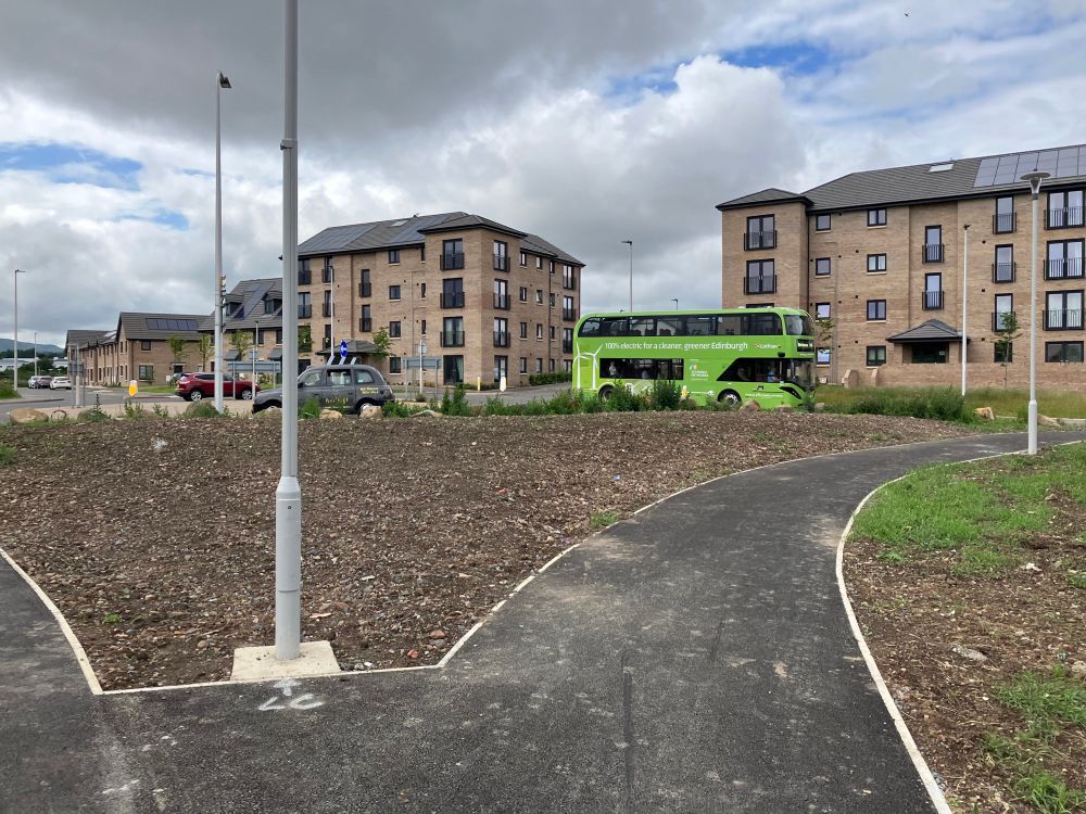 Fork in new path looking back at Greendykes Rd with electric bus and new housing with solar panels in background (and Royal Infirmary of Edinburgh in distance on left)