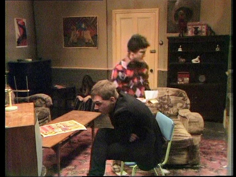 The fifth housemate from The Young Ones. She's sitting on the floor next to the door. 
