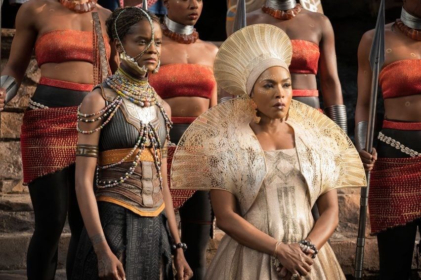 Still from Black Panther, showing the tribes watching T'Challa be crowned. The characters are all dressed in costumes inspired by traditional African dress, with bright fabrics, beads, and dramatic shapes. 