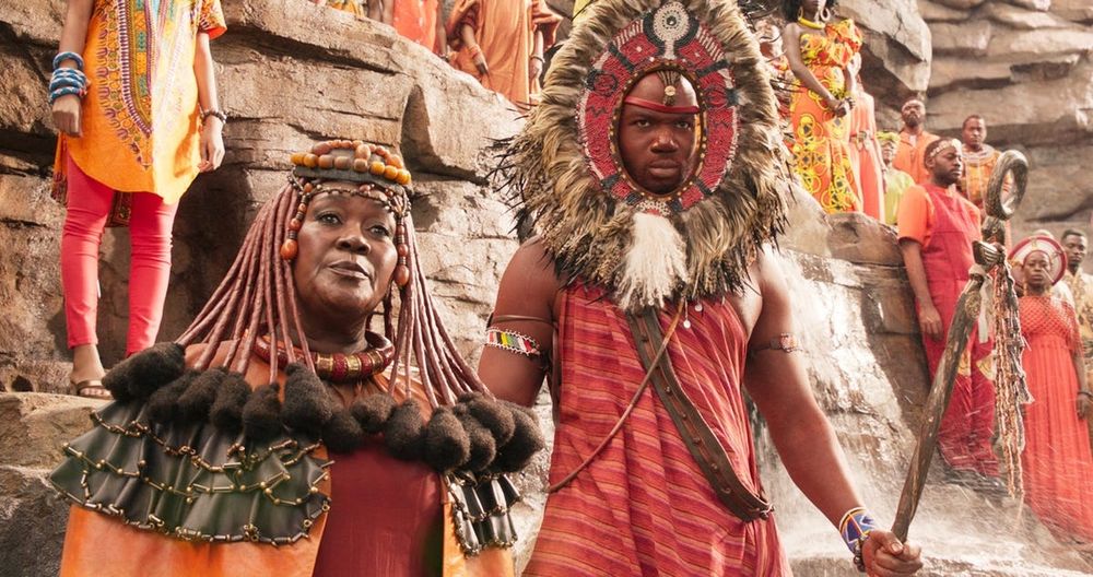 Still from Black Panther, showing the tribes watching T'Challa be crowned. The characters are all dressed in costumes inspired by traditional African dress, with bright fabrics, beads, and dramatic shapes. 