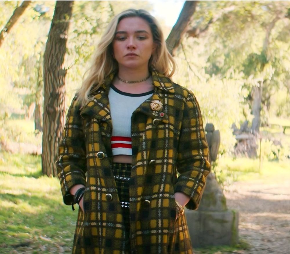 Yelena is wearing a yellow plaid coat with a white cropped tshirt and check trousers. She looks very grunge cool.