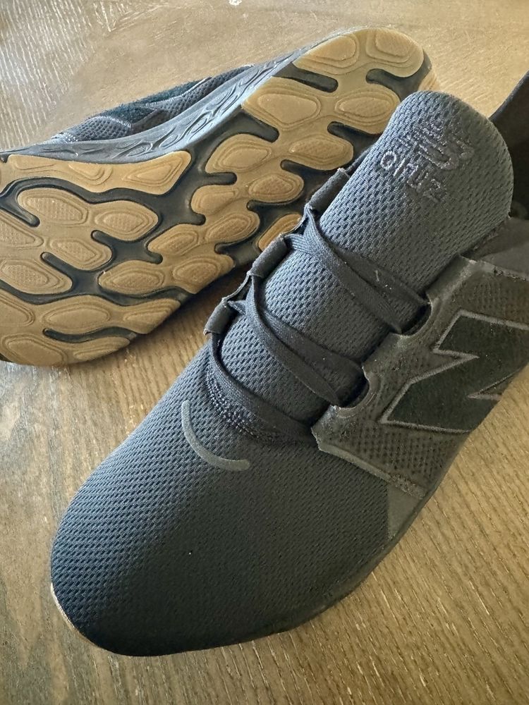 A pair of black athletic shoes with textured soles is placed on a wooden surface.