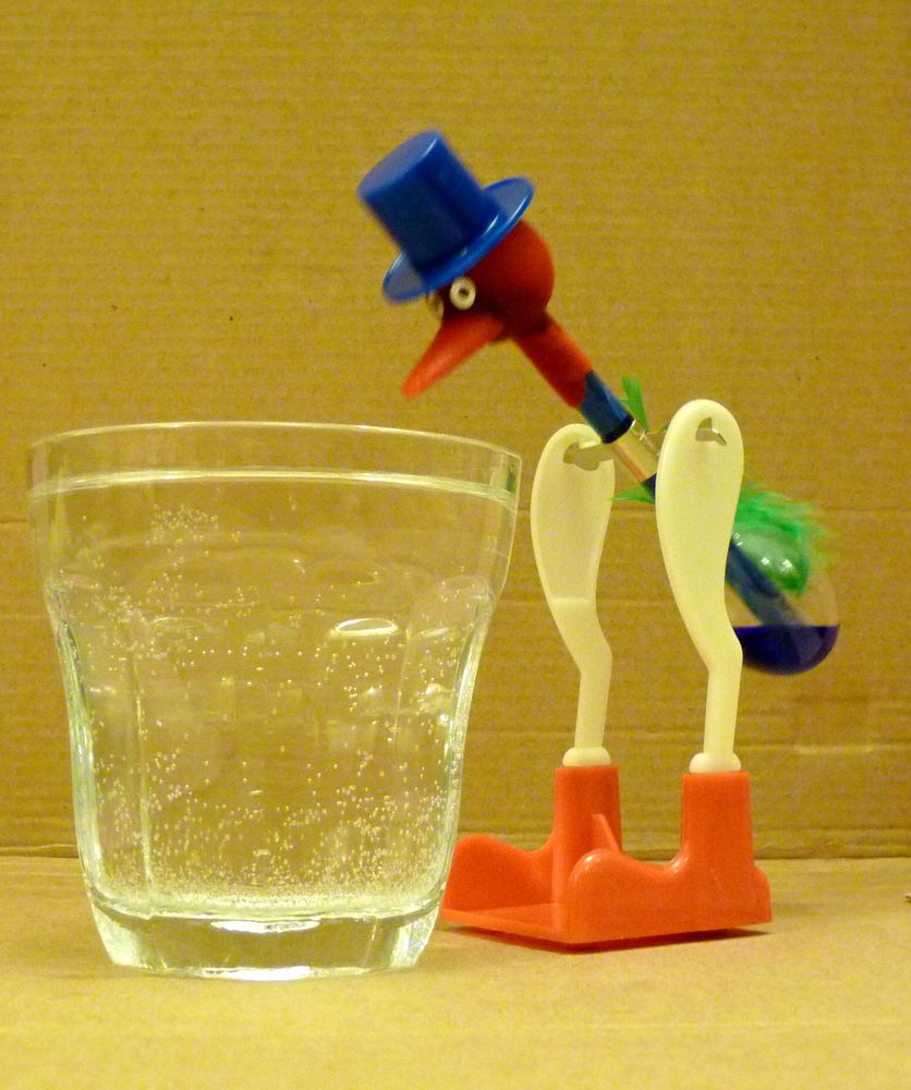 A photo of a plastic “Dipping Bird” toy beside a glass of water.