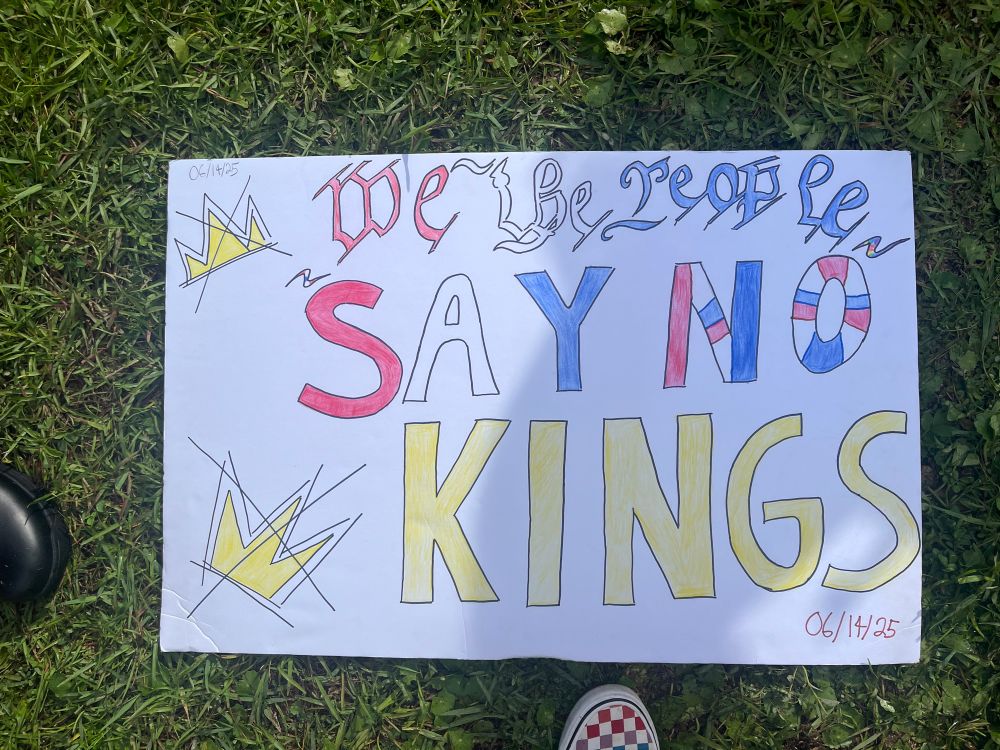 A protest sign with yellow crowns with x’s in the middle of them with the words “We The People Say No Kings” written on it 