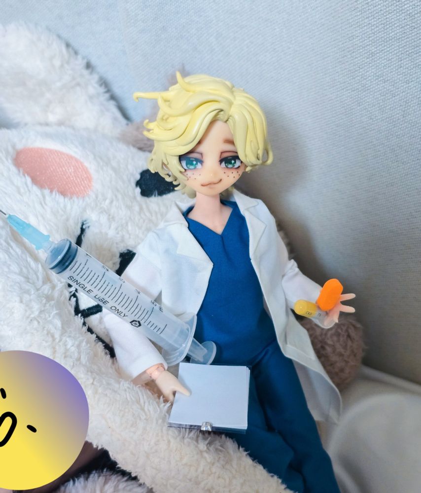 양 얼굴이 그려진 모자에 기대고 있는 인형. 흰 가운 의사 복장을 하고 있다. 주사와 차트를 들고 다른 손에는 주황색 알약을 두 개 들고 있다.