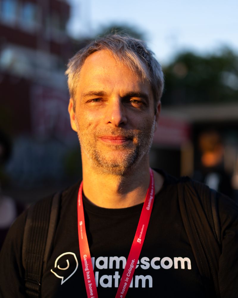 A portrait of Gustavo Steinberg, CEO of Gamescom Brazil / Gamescom Latam. The sun is hitting his face nicely from the left giving the picture a beautiful warmth. He is wearing a black shirt of Gamescom Latam. 