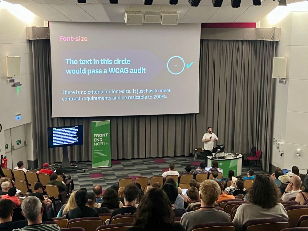 Craig on stage. Text in a tiny tiny circle which does pass WCAG!