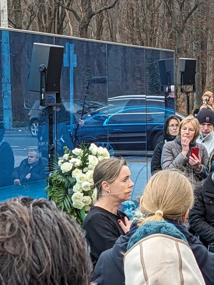 Menschen vor einer blauen Wand, Blumenkranz, Lautsprecher