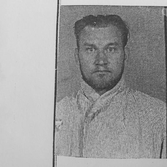 Auf dem Foto ist das Porträt eines Mannes zu sehen. Er hat einen volleren, rundlichen Gesichtszuschnitt mit deutlichen, markanten Gesichtszügen. Seine Haare sind kurz und erscheinen etwas unordentlich, möglicherweise wellig, und er trägt keinen sichtbaren Bart oder Schnurrbart. Seine Augenbrauen sind dicht und dunkel, was seine intensiven, weit geöffneten Augen unterstreicht. Der Blick des Mannes ist direkt in die Kamera gerichtet, mit einem Ausdruck, der als nachdenklich oder möglicherweise besorgt interpretiert werden könnte. Der Mann trägt ein Hemd mit einem groben, sichtbaren Webmuster, allerdings ist nur ein Teil des Kragens erkennbar