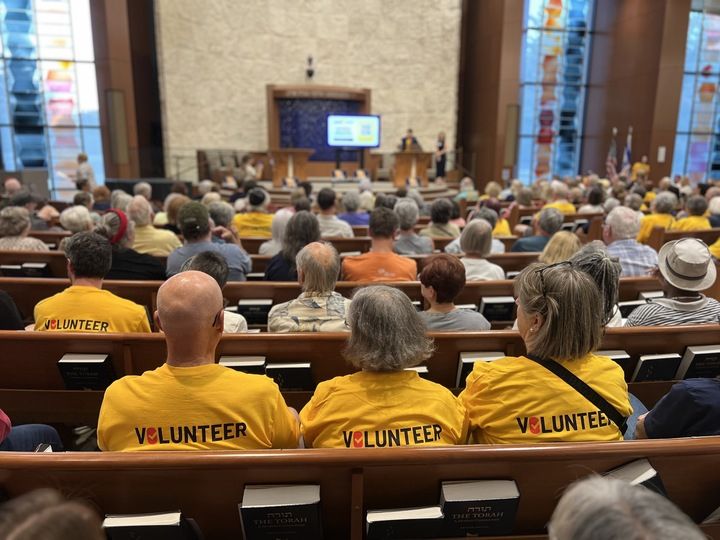 Three volunteers wearing yellow shirts that say "Volunteer" on the back listen to speakers at the St. Louis launch event for Respect MO Voters. 
