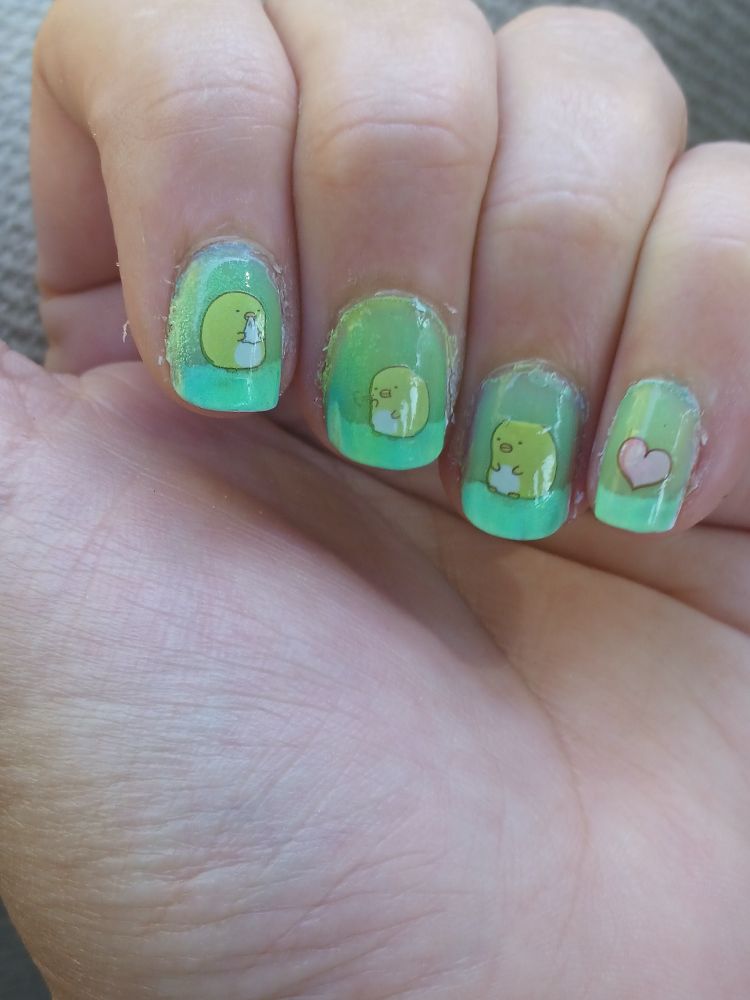 A green French tip manicure. Each nail is decorated with a different decal of a Sanrio sumikko gurashi character named "Penguin?". There is a small pink heart on the pinky nail.