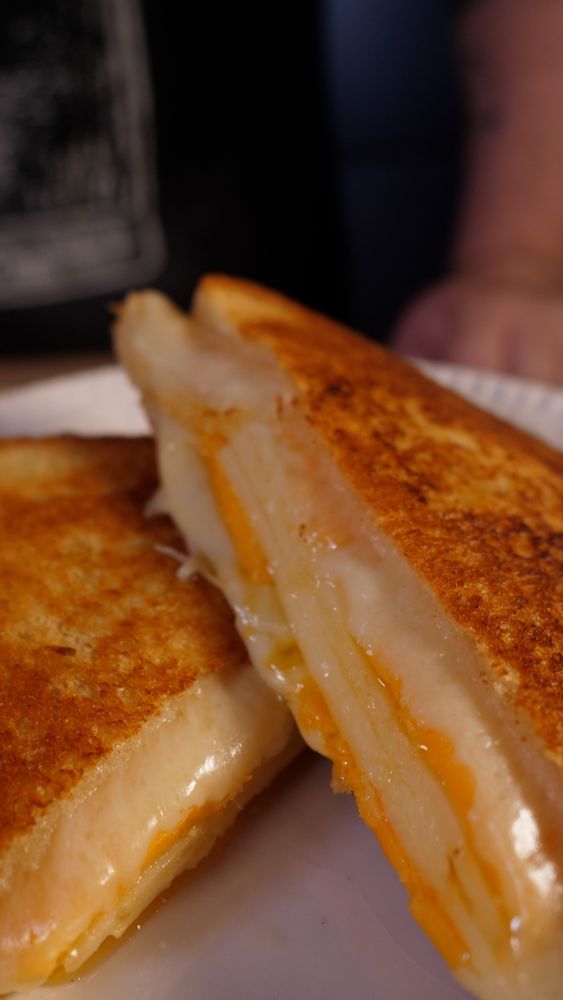 Une photographie d’un grilled cheese maison, un sandwich grillé et doré au beurre, garni de cheddar, de comté et d’emmental. Il illustre une recette postée en lien video