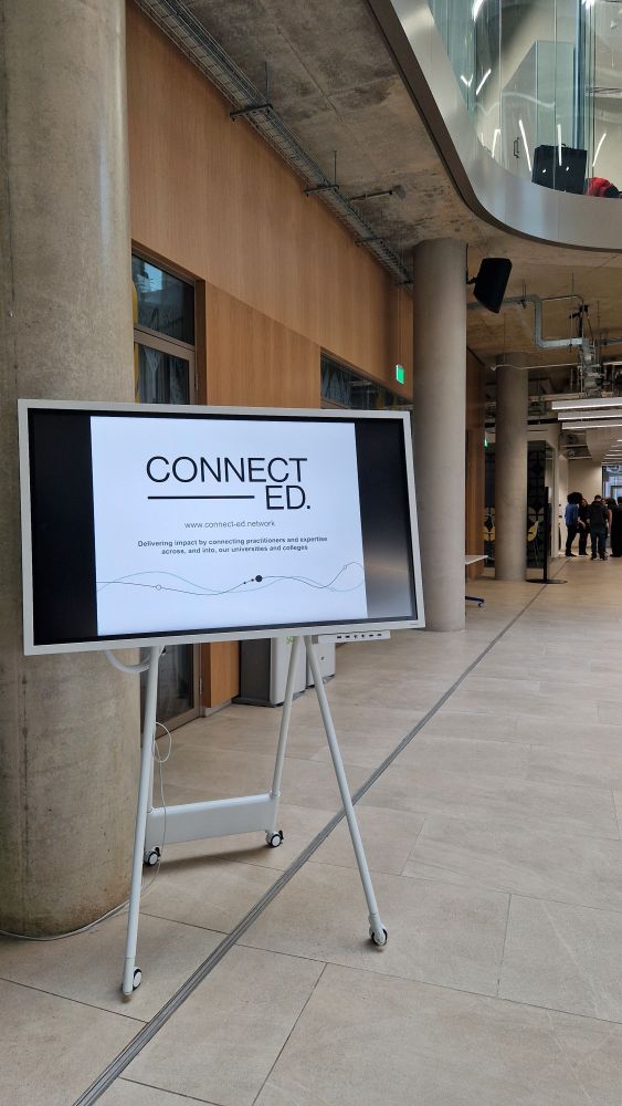 A sign with CONNECT-ED branding visible, people standing in distance, in room/corridor with concrete pillars