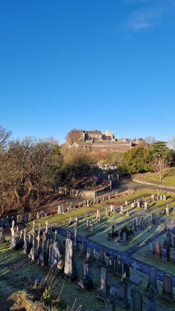 Graveyard in foreground, (Stirling) Castle on hill in background, clear blue sky