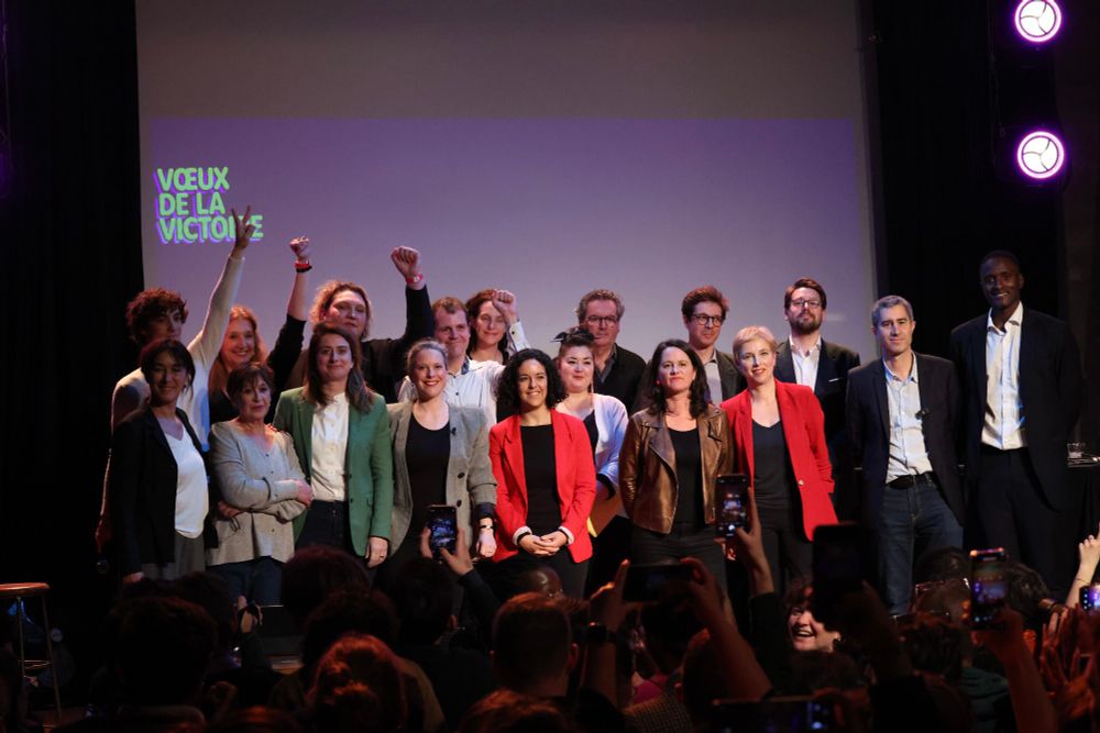 Une vingtaine de personnes sont sur scène, debout, devant de nombreuses personnes. 
Derrière un écran où est indiqué Vœux de la victoire 