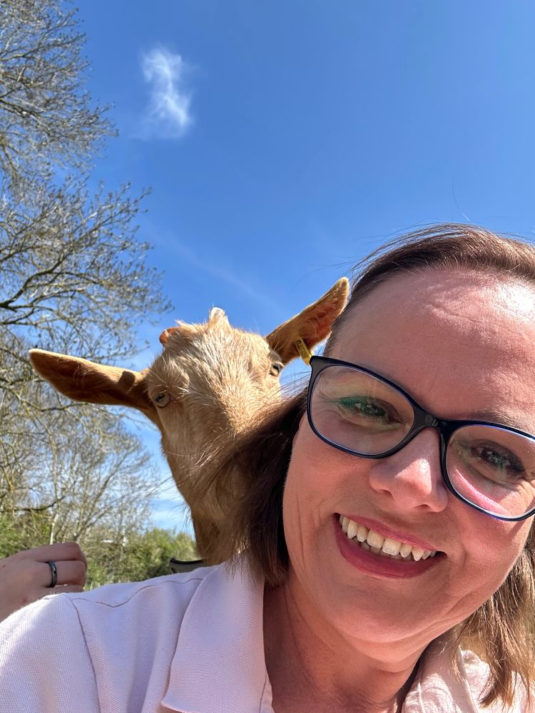 Me with a huge grin and a cute cheeky goat peeking over my shoulder nibbling my hair