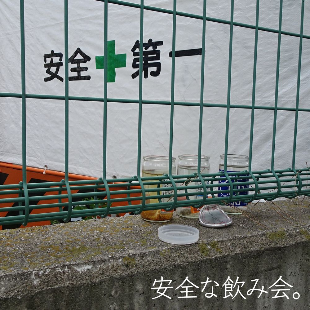 「安全な飲み会」工事現場の「安全第一」のシートの前に飲み捨てられた酒のコップが並んでいる。