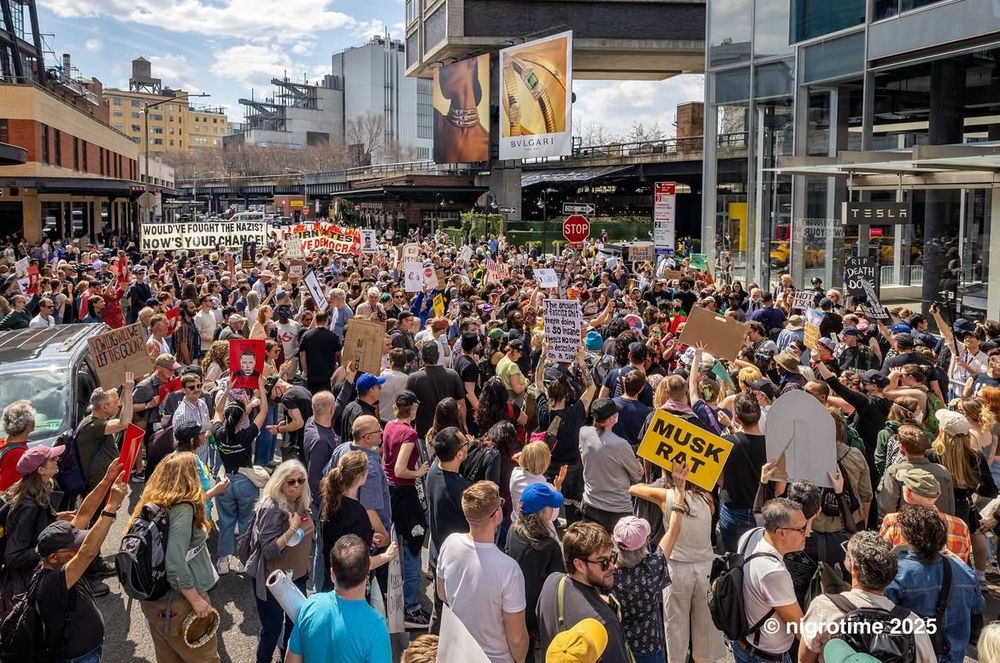 Photo of people protesting at Tesla in the meatpacking district in manhattan, Saturday march 29, 2025. Thousands of people in the streets with colorful signs against Elon Musk. 

Blue sky with fluffy white clouds. 

Photo by Michael Nigro. 