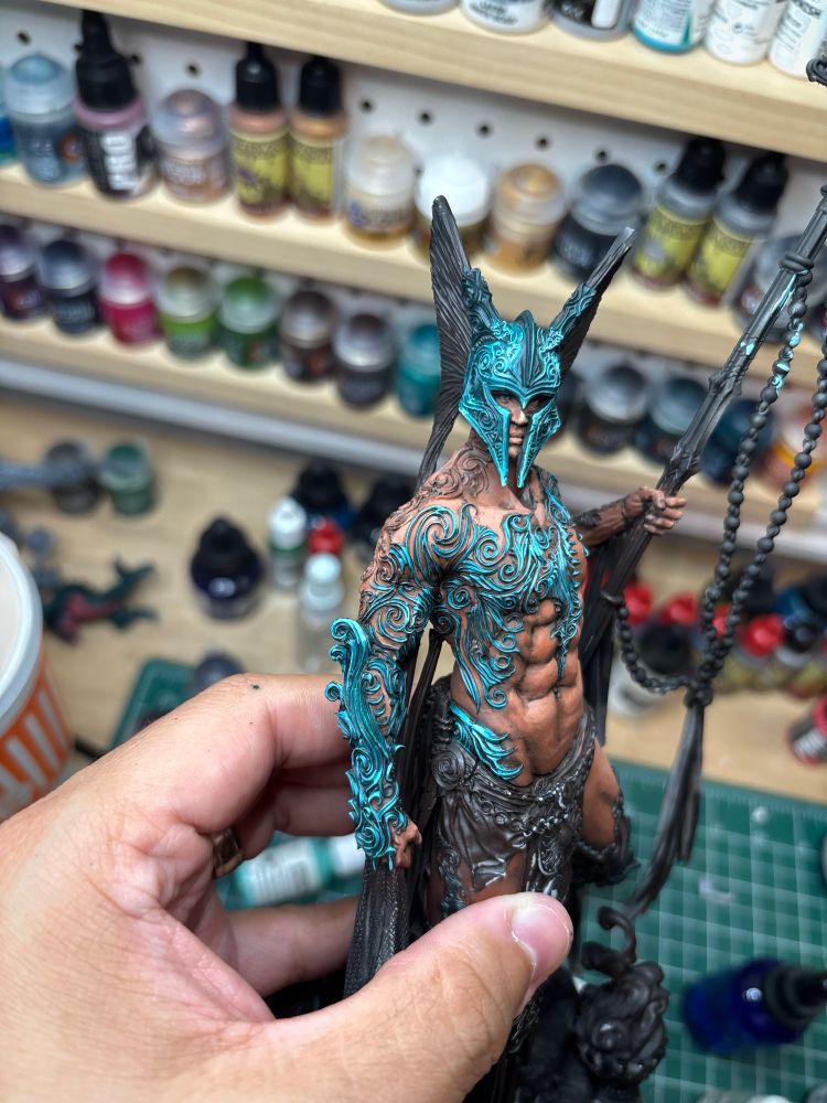 Titan of body miniature partially painted. Skin tones laid down over black and brown primer. Human figure with armor accessories, posed standing on a rock, wearing a helmet and holding a spear. The armor is a soft green and white non metallic metal. Picture from the front