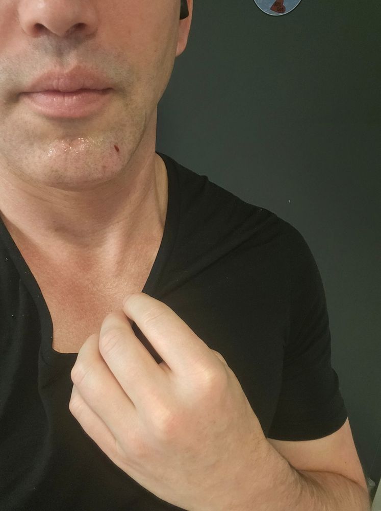 A close-up of a human with their hand on the collar of their wool t-shirt.
