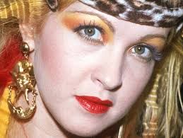 Cyndi Lauper in an iconic coral lip, gold and orange eyeshadow, leopard hair wrap, gold doorknocker earrrings