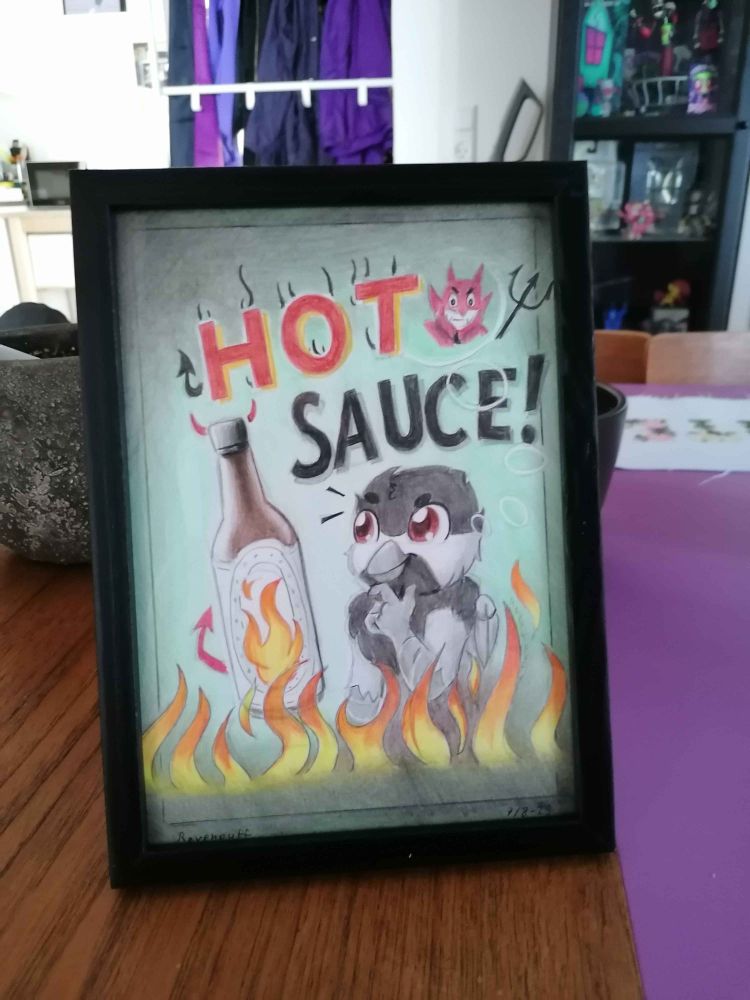 Photo of the framed hot sauce Burd art standing up on a table. 