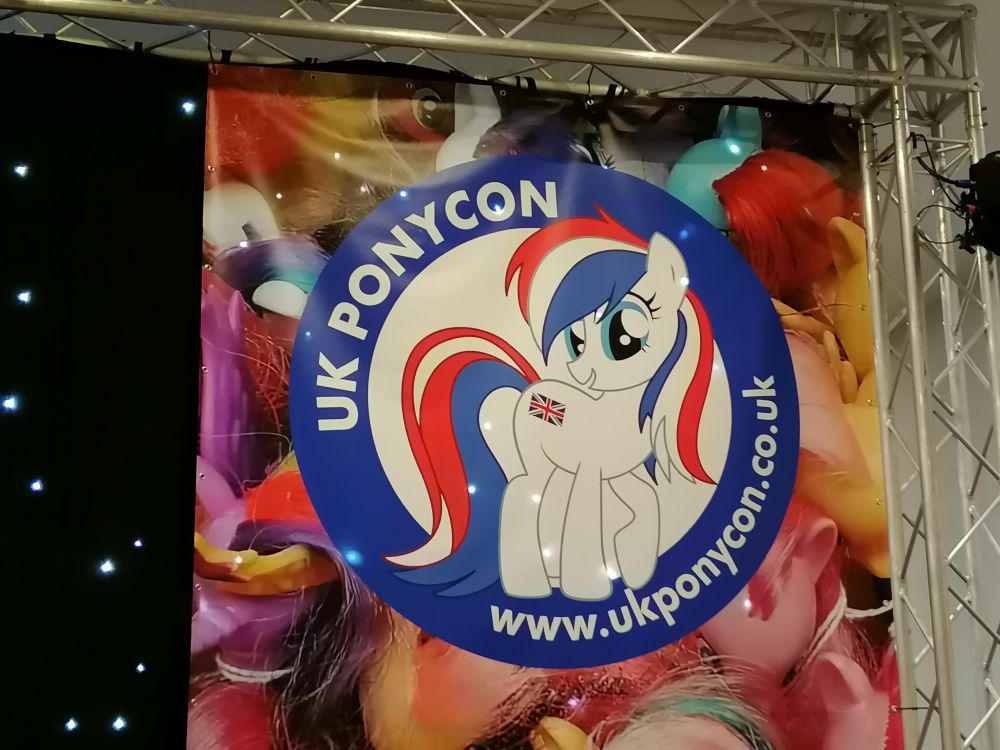 Photo of the UK PonyCon mascot Britania. A white coated earth pony with red, white and blue striped mane and tail. Union Jack as cutiemark 