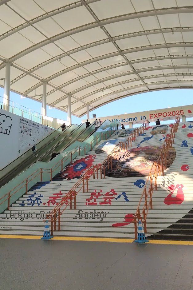 夢洲駅改札外のでかい階段。両端にエスカレーターがあるがこの写真では左側のものしか写っていない。これを上ると東ゲート前の広い空間に出る。