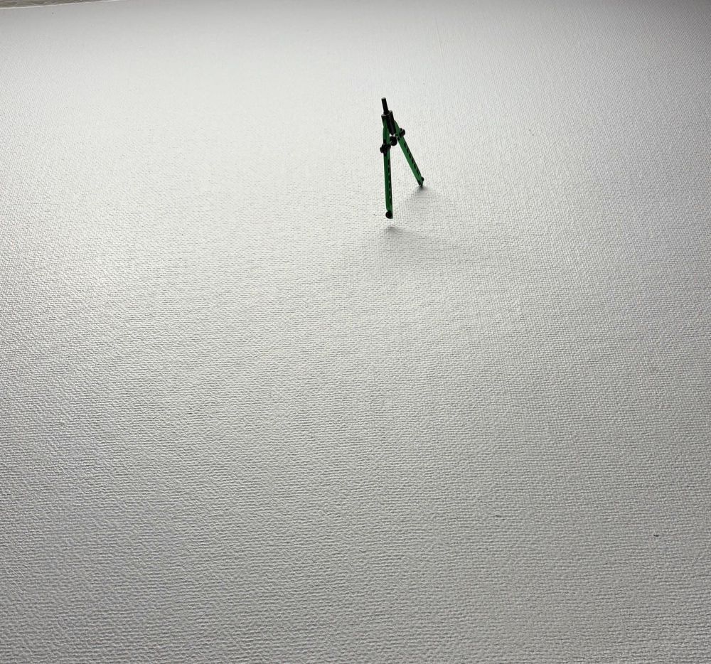 Foto von einer Wand in der ein Zirkel mit der Spitze steckt. 