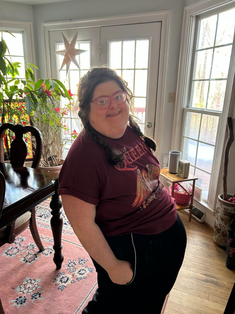 Sara Ruh born with Down syndrome is an avid tech user.  She is wearing black slacks, a Queen shirt, and has braids.
