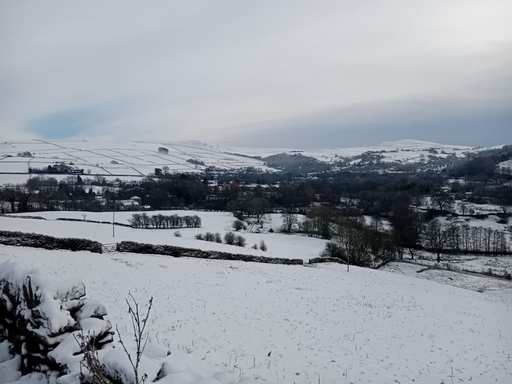 View of Hayfield with surrounding fields and hills under snow.