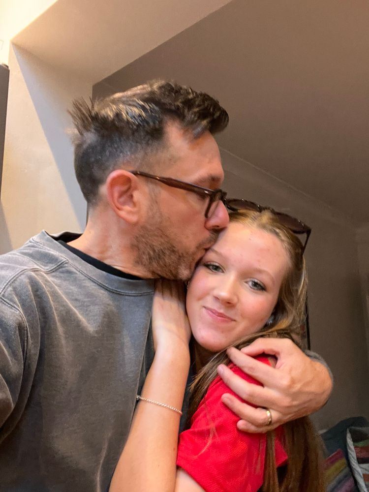 A selfie of me hugging my teenage daughter and kissing her on the forehead.