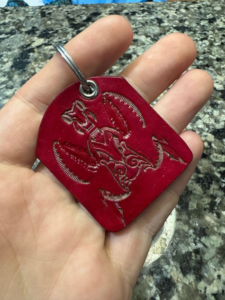 A handmade leather keychain. The keychain is red and has a praying mantis embossed into the surface