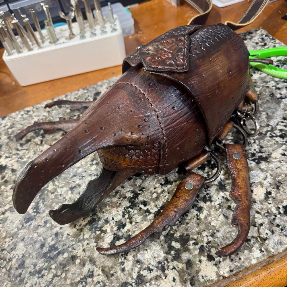 A handmade leather beetle bag laying on a granite slab
