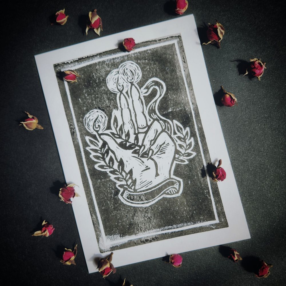 Linocut of a hand of Glory holding a vine and surrounded by a ribbon with three lit fingers 