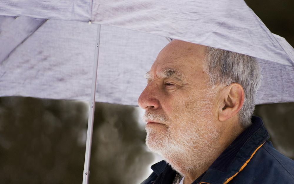 Pensive older man looking into the distances from under his umbrella