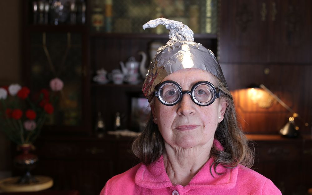 Woman with thick, round, black eye glasses wearing tin foil hat