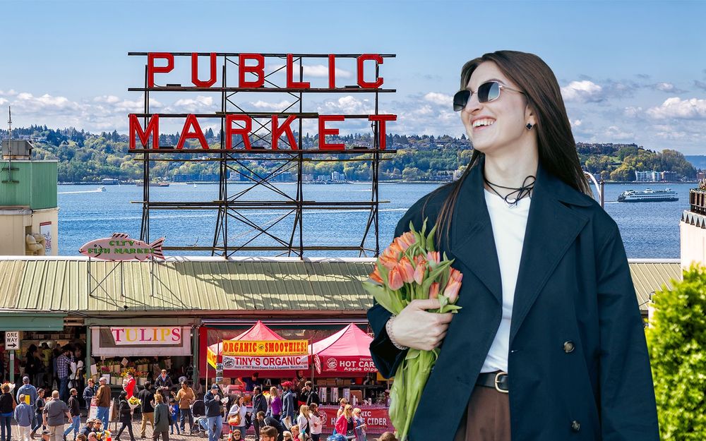 Smiling woman wearing sunglasses holding tulips on bright sunny day at Pike Place Market, "Public Market" sign with expansive view behind of ferry crossing sparkling water and green West Seattle