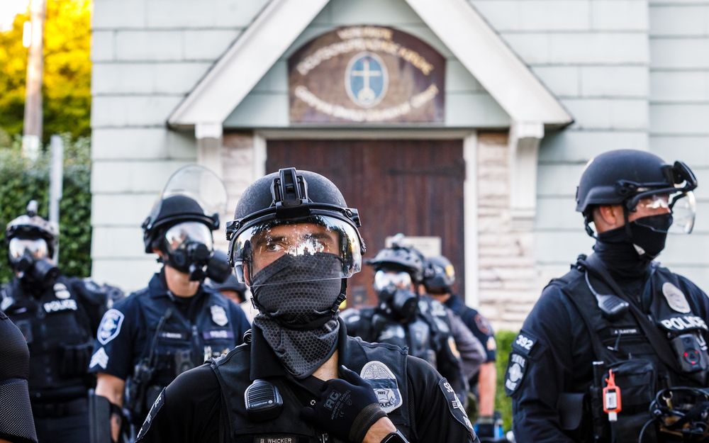 Crowd of SPD cops in riot gear heading into Cal Anderson Park with Calvary the Hill Church in the background