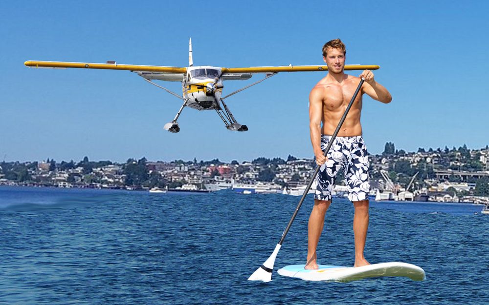 Seaplane about to land on Lake Union right behind tan, happy, handsome man paddleboarding in board shorts and no shirt. 